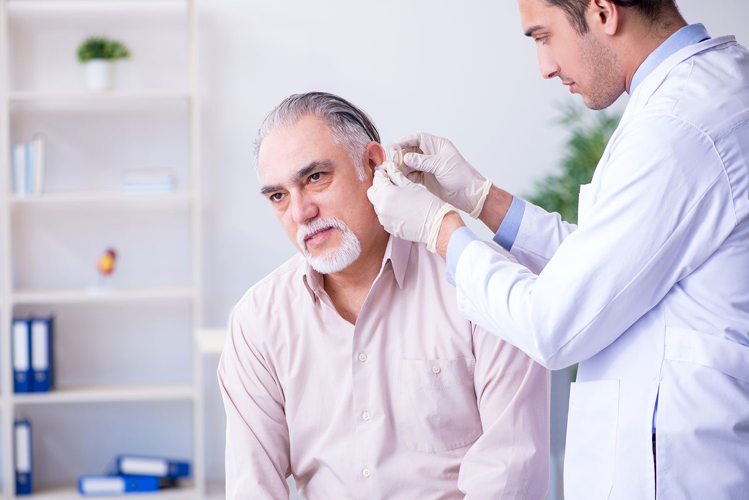Otolaryngologist fitting a male patient with hearing aids